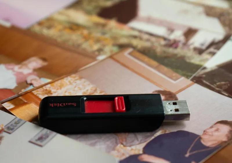 USB drive resting on spread of old family photos ready for digital delivery